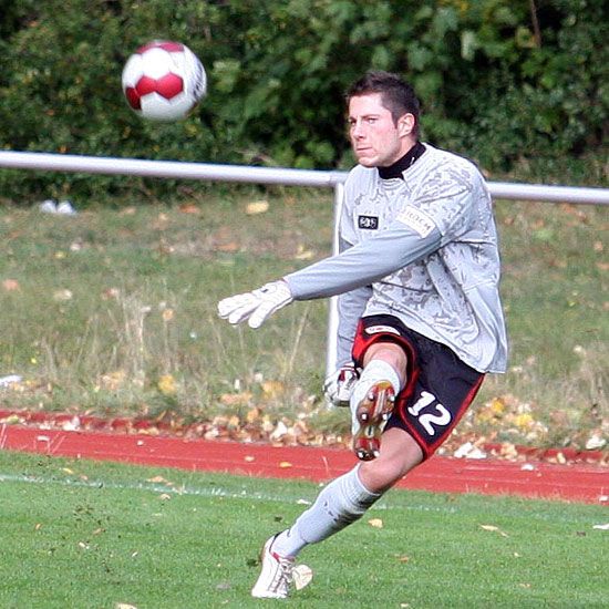 Ein Fußballtorwart in grauem Trikot und Handschuhen führt einen Abschlag aus, während der Ball in der Luft fliegt.