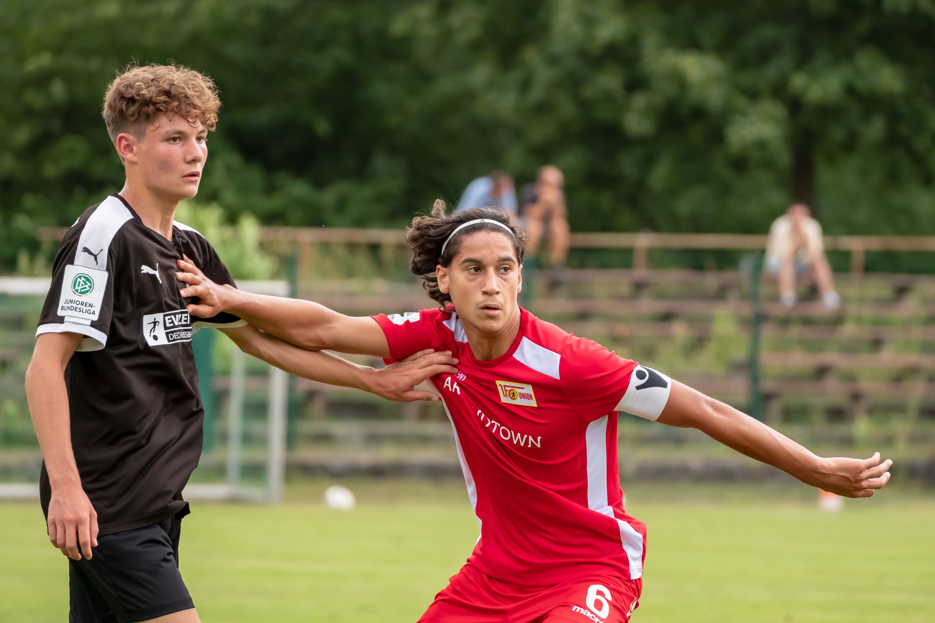 Zwei junge Fußballspieler im Wettkampf; einer in roter und einer in schwarzer Uniform. Ein Spieler versucht, den anderen zu blockieren.