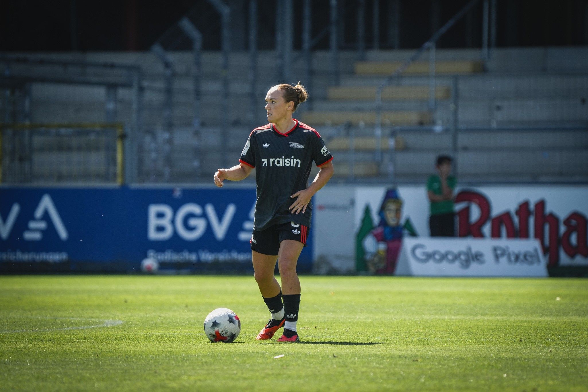 Spieler in einem schwarzen Trikot mit dem Schriftzug "raisin" steht auf einem Fußballfeld und Dribbelt den Ball.