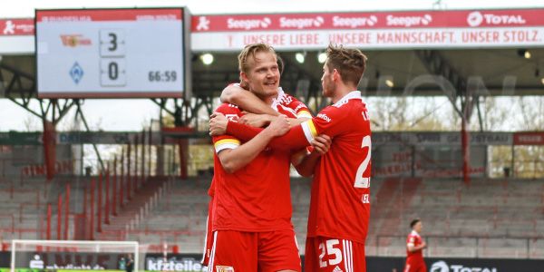 Players of 1. FC Union Berlin celebrate a goal surrounded by cheering fans in the stadium.