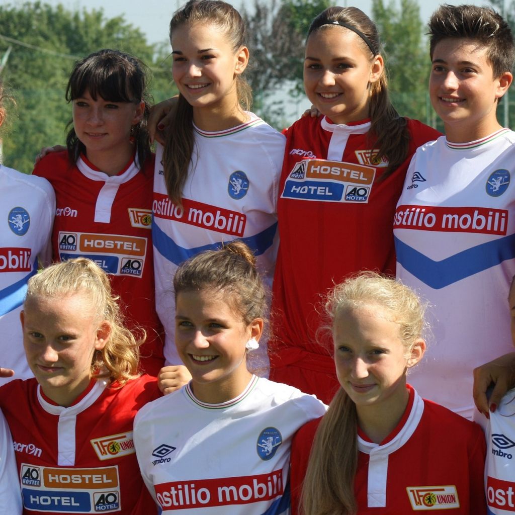 Mädchen in Fußballtrikots posieren lächelnd in einer Gruppe im Freien.