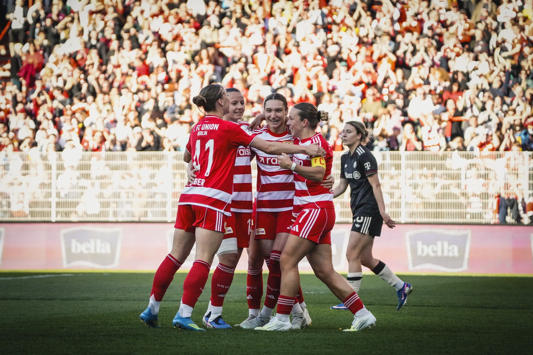 Spielerinnen einer Fußballmannschaft feiern einen Torerfolg vor jubelndem Publikum im Hintergrund.