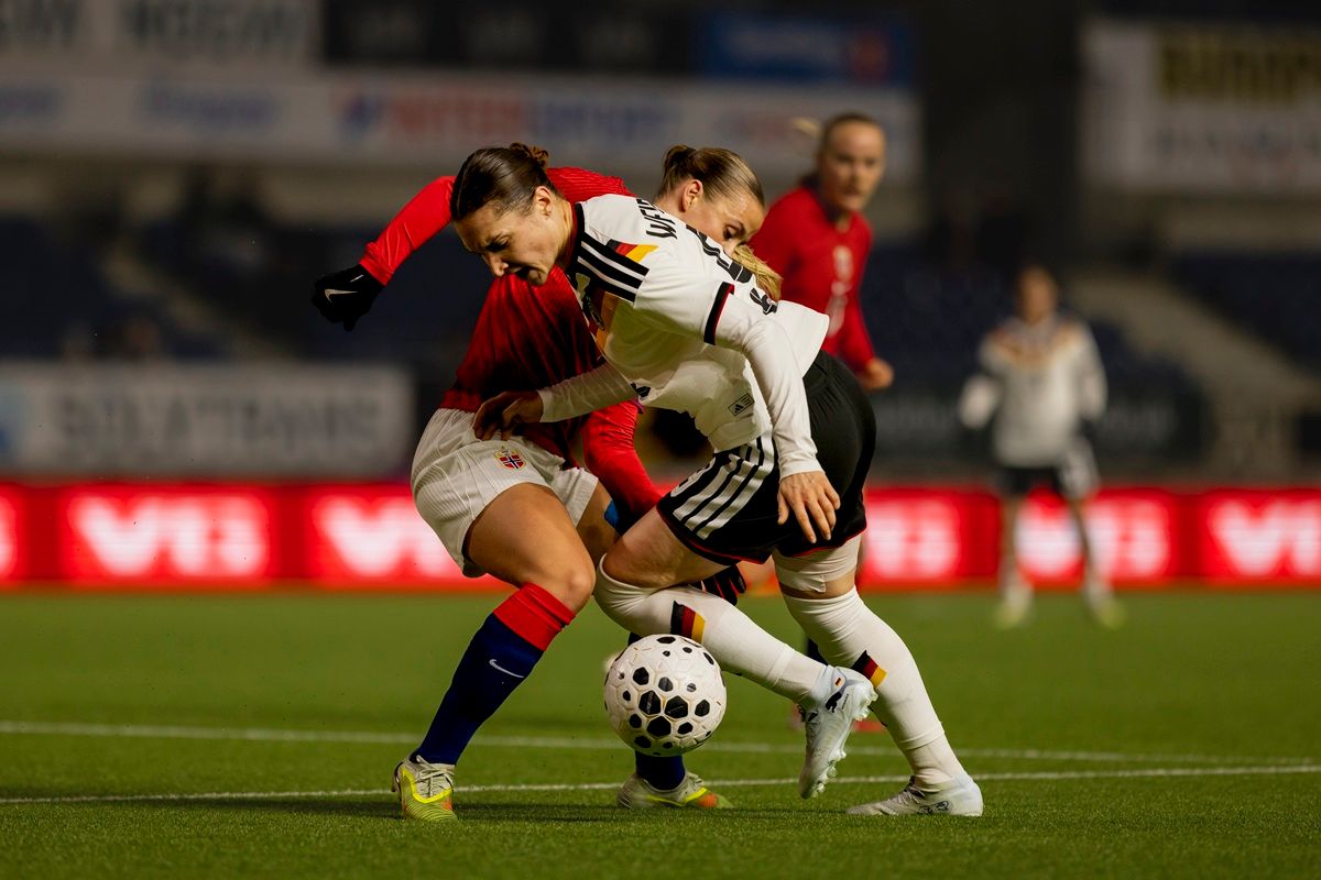 Zwei Fußballspielerinnen kämpfen um den Ball während eines Spiels auf einem beleuchteten Feld.