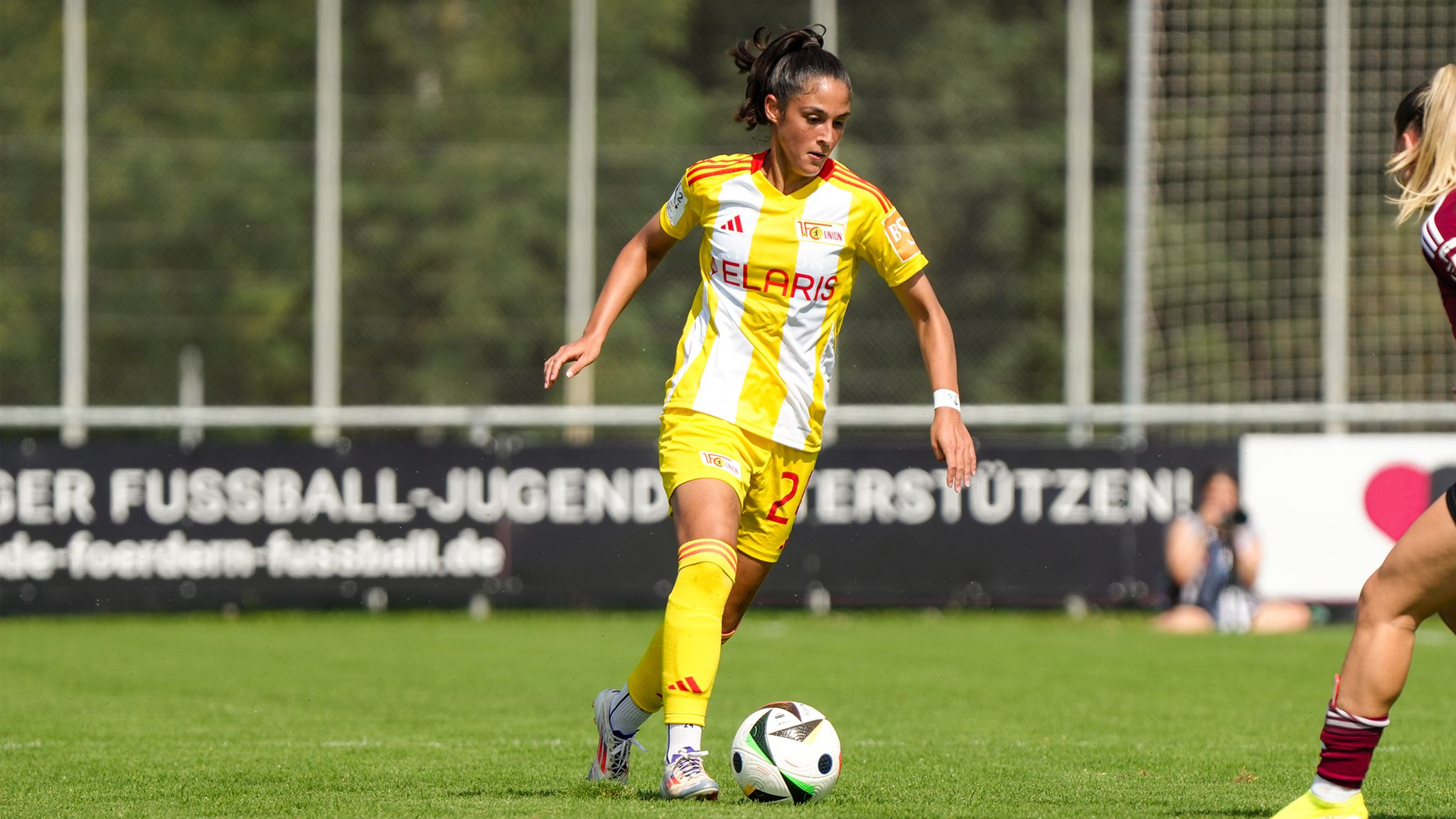 Eine Fußballspielerin in gelb-weißem Trikot dribbelt mit einem Ball auf einem grünen Spielfeld.