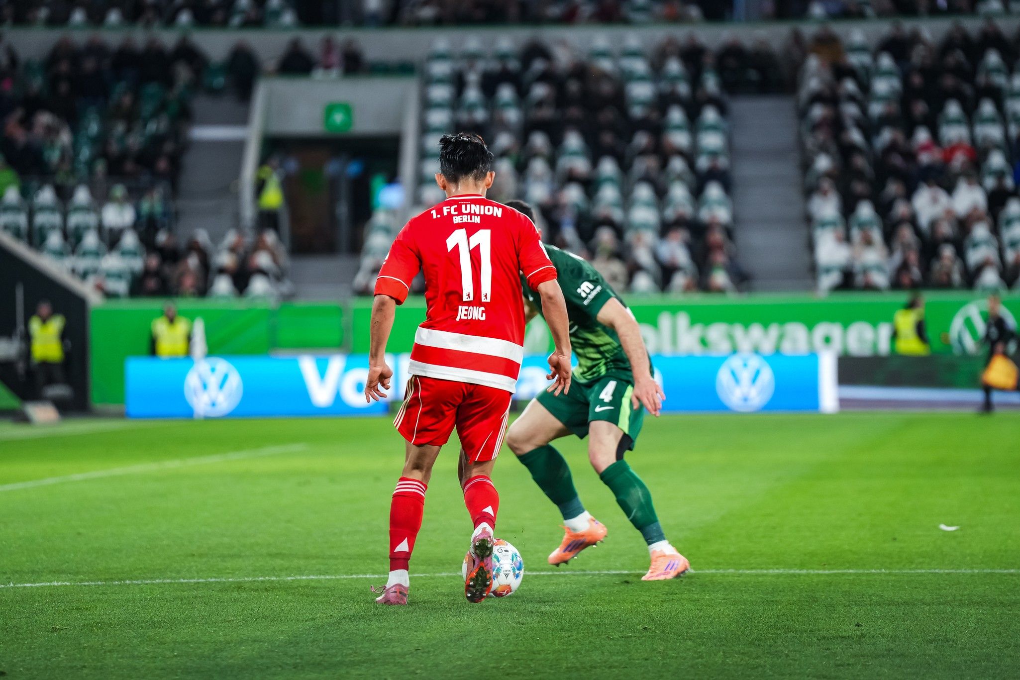 Spielszene im Fußballstadion, ein Spieler in rotem Trikot mit der Nummer 11 bereitet sich auf einen Freistoß vor.