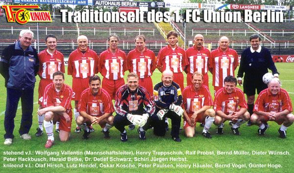 Gruppe von Fußballspielern in roten Trikots posiert für ein Mannschaftsfoto, umgeben von einem Stadionhintergrund.