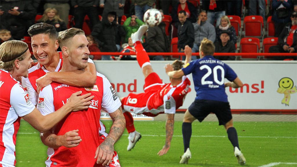 Fußballspiel mit jubelnden Spielern von Union Berlin nach einem Tor, während ein Gegner einen Schuss abgibt.