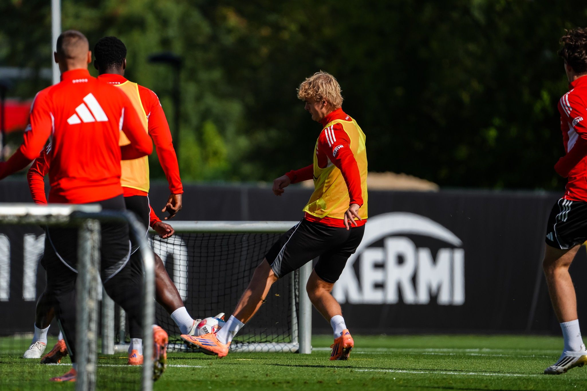 Spieler in roten Trainingsanzügen üben im Freien, während einer einen Ball ins Tor schießt.
