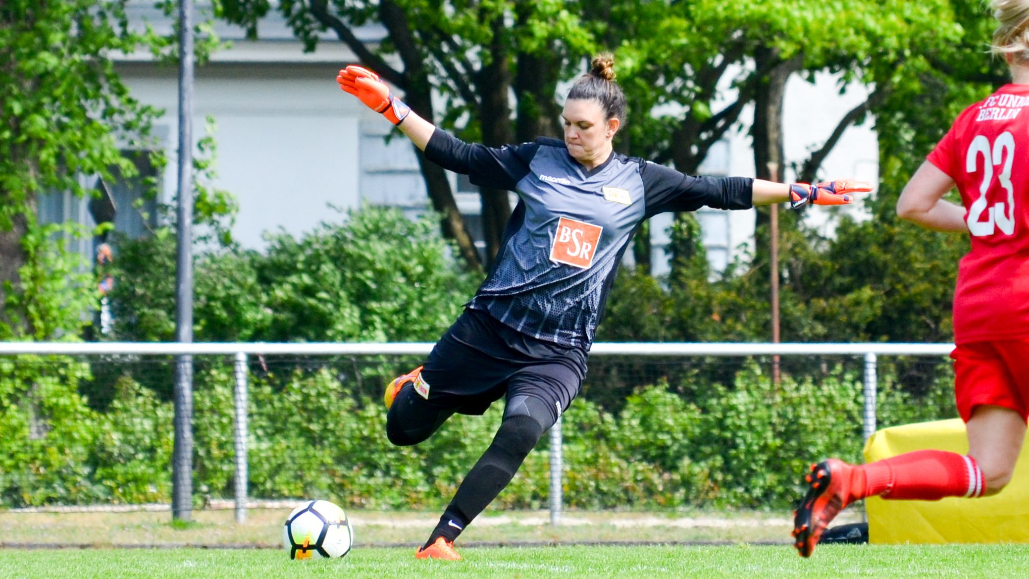 Torhüterin in schwarzer Sportbekleidung hält mit beiden Händen den Ball und bereitet sich auf einen Abschlag vor.