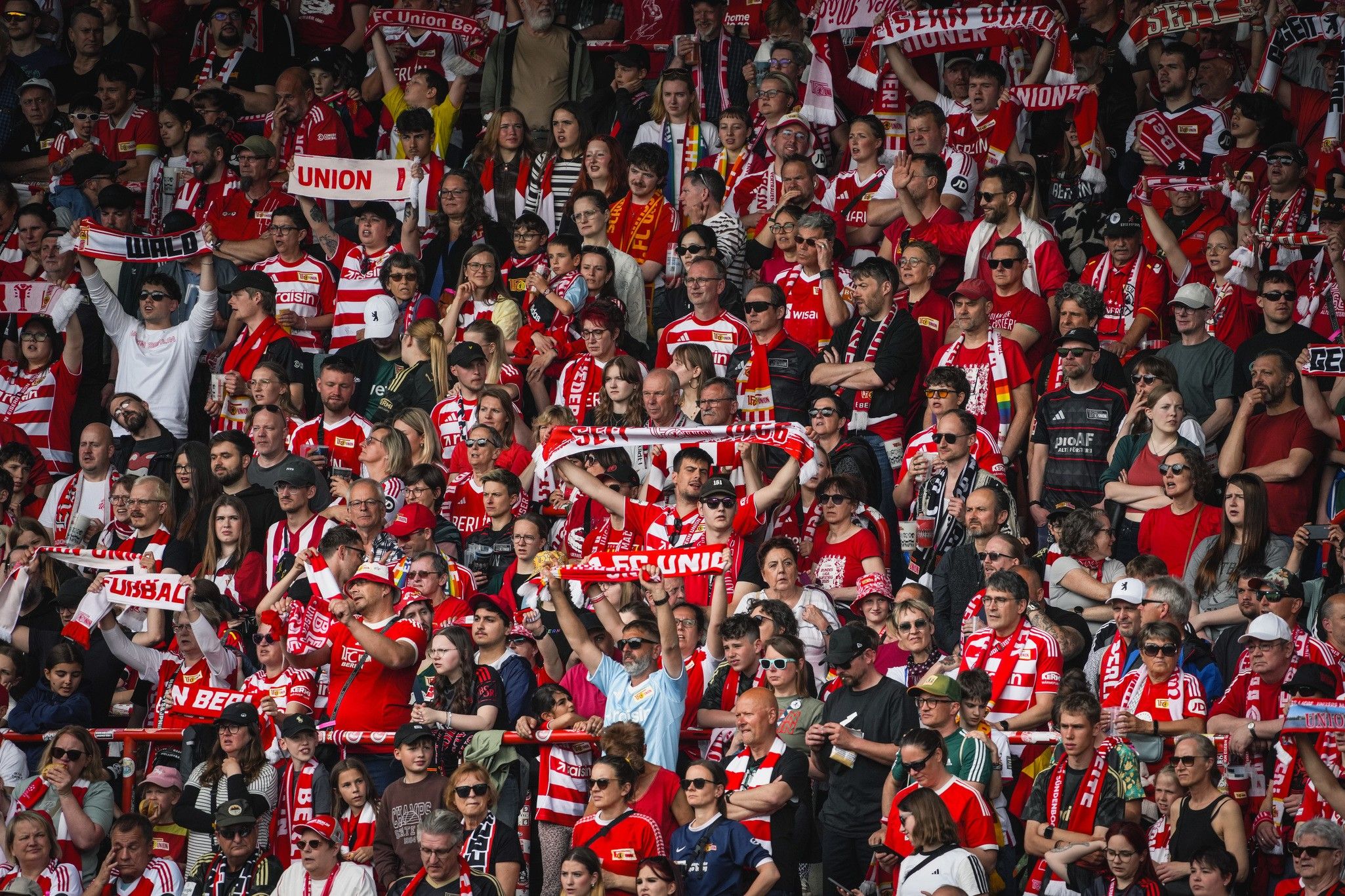 Eine große Menge von Fans in rot-weißen Trikots feiert in einem Stadion, einige halten Schals und Fahnen hoch.
