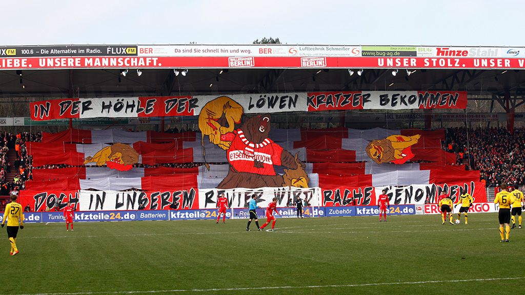 Großes Stadionbanner mit rot-weißen Farben und einem Bärenmotiv, begleitet von der Aufschrift in deutscher Sprache.