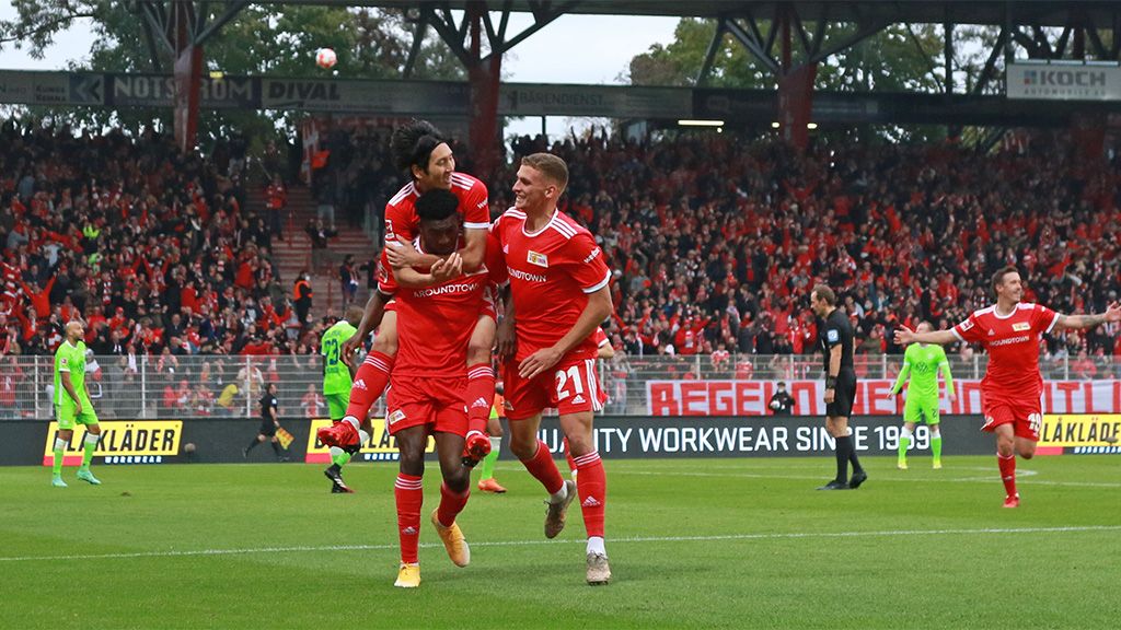 Spieler in roten Trikots feiern ein Tor vor begeisterten Fans im Stadion.