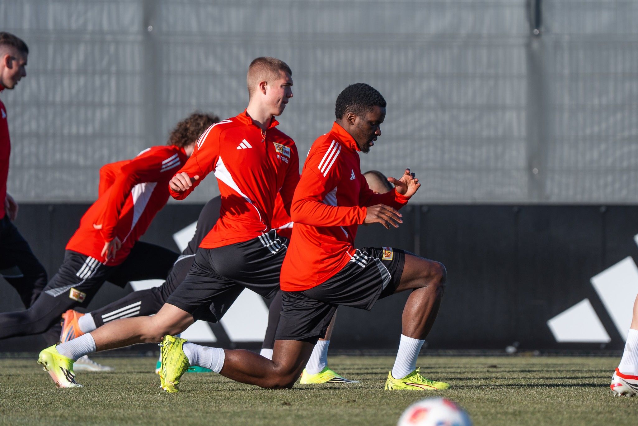 Fußballspieler in roten Trainingsanzügen führen Übungen auf einem Platz durch.