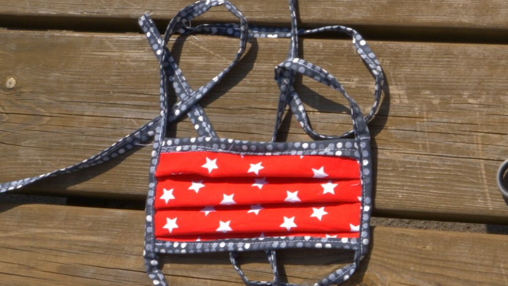 Rote Maske mit weißen Sternen, auf einem hölzernen Tisch liegend, mit Bändern zur Befestigung.