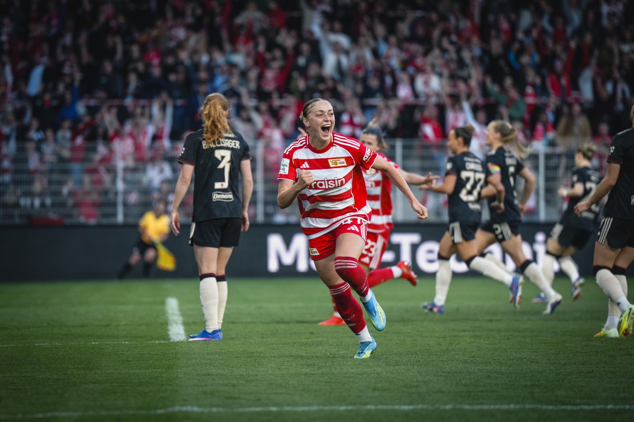 Spielerin von Union Berlin jubelt nach einem Tor, umgeben von feiernden Teamkolleginnen und jubelnden Fans im Stadion.