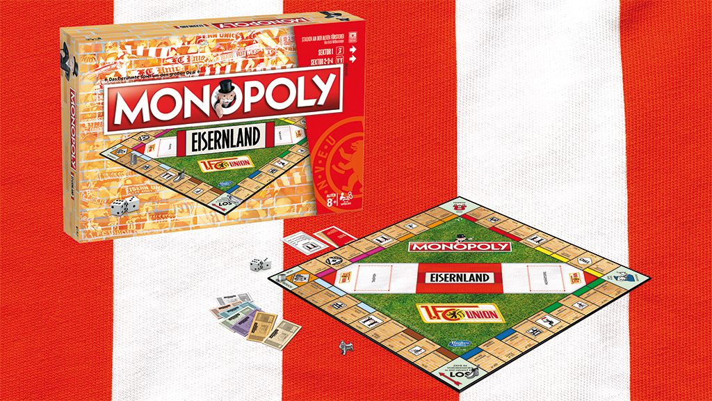 Monopoly-Spiel mit der Version "Eisenland", inklusive Spielbrett, Würfeln, Spielfiguren und Spielkarten auf einem rot-weißen Hintergrund.