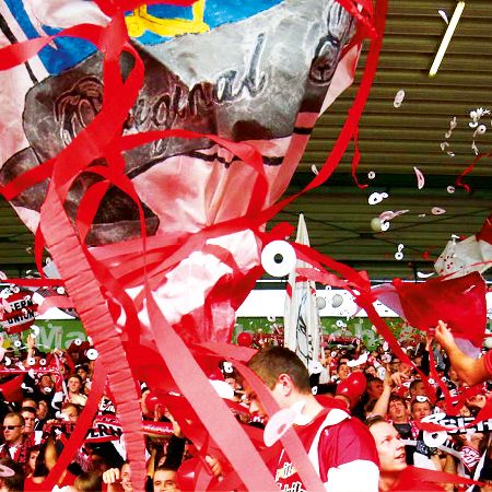 Menschenmenge in einem Stadion mit roten Fähnchen und Konfetti, die eine Sportveranstaltung feiern.