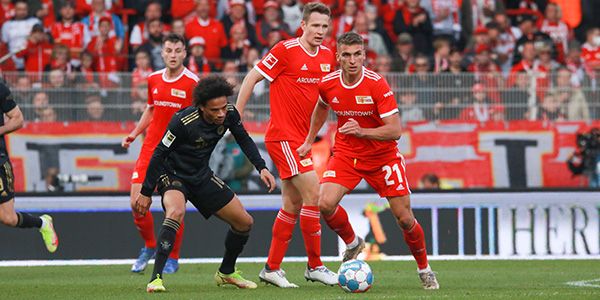Game scene of a football match with players in red and black jerseys fighting for the ball, showing a tense atmosphere.