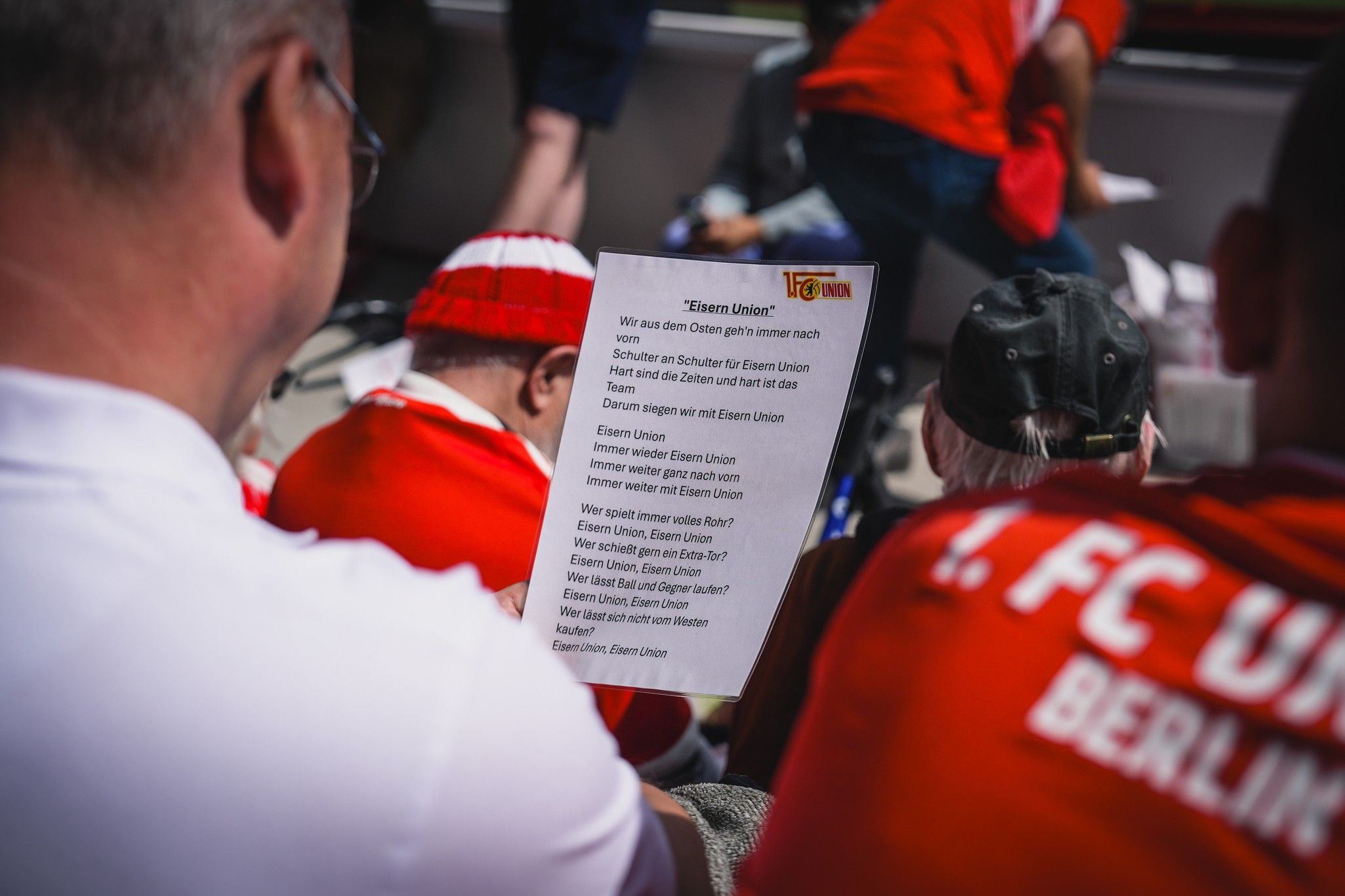 Ein Gruppenevent mit Fans des 1. FC Union Berlin, die eine Liedzeile auf einem Blatt Papier lesen.