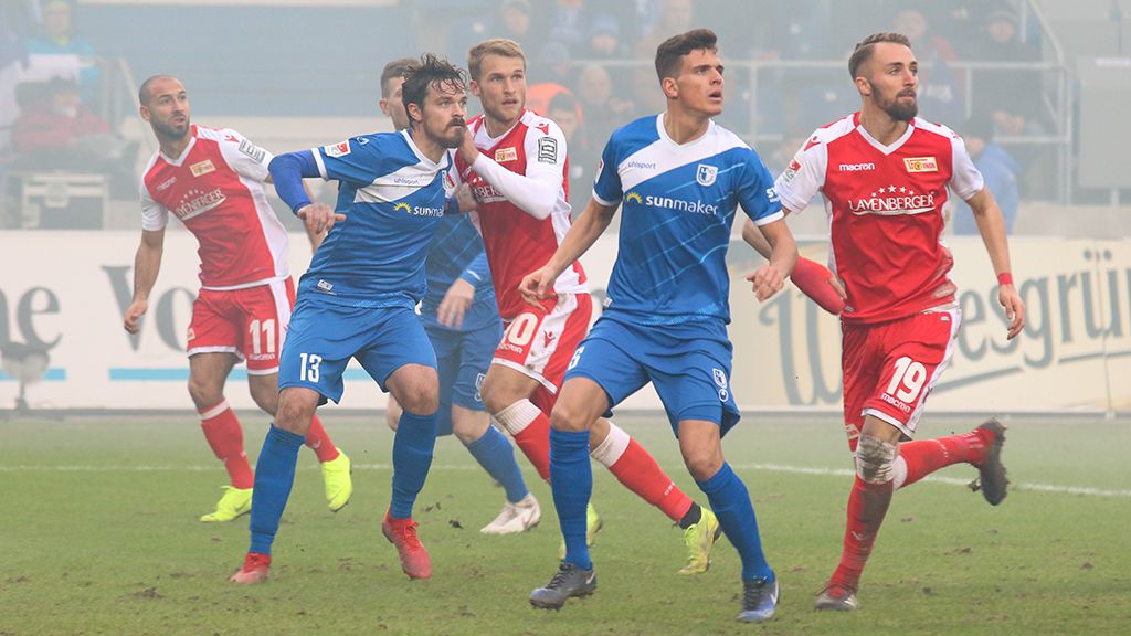 Two teams in a soccer match, players in blue and red jerseys chase the ball on a foggy field.