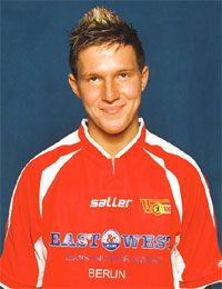 Mann mit kurzem, blonden Haar in einem roten Fußballtrikot vor einem blauen Hintergrund.