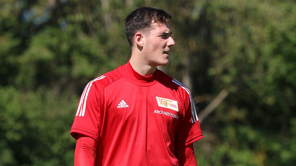 A young man is wearing a red sports jersey during outdoor training, surrounded by trees.
