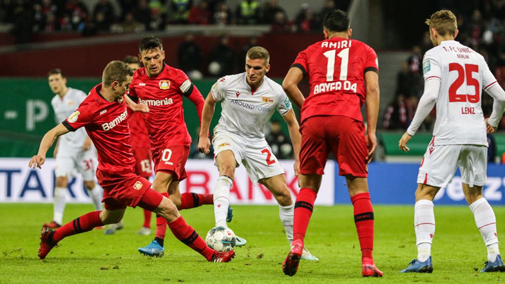 Spielszene eines Fußballspiels mit Spielern von Bayer Leverkusen und Union Berlin im konzentrierten Wettkampf um den Ball.