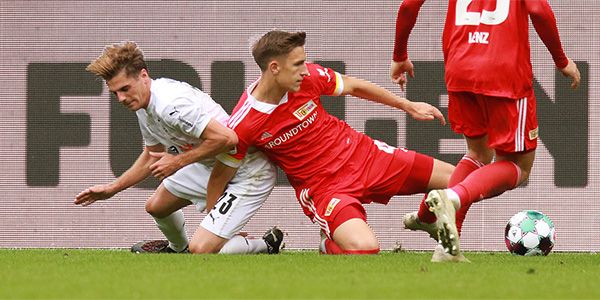 Two soccer players are fighting for the ball, one falls to the ground while the other kicks it.