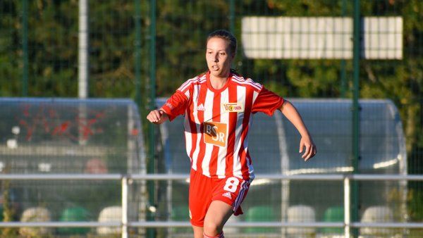 Soccer player in a red jersey with white stripes runs energetically across the field.