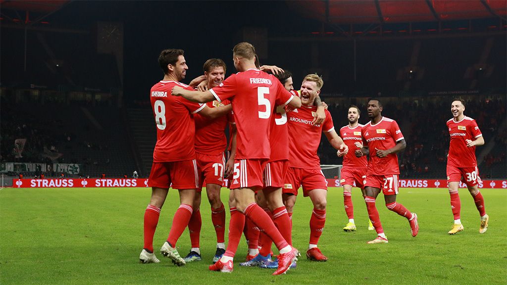 Fußballmannschaft in roten Trikots feiert einen Torerfolg auf dem Spielfeld.