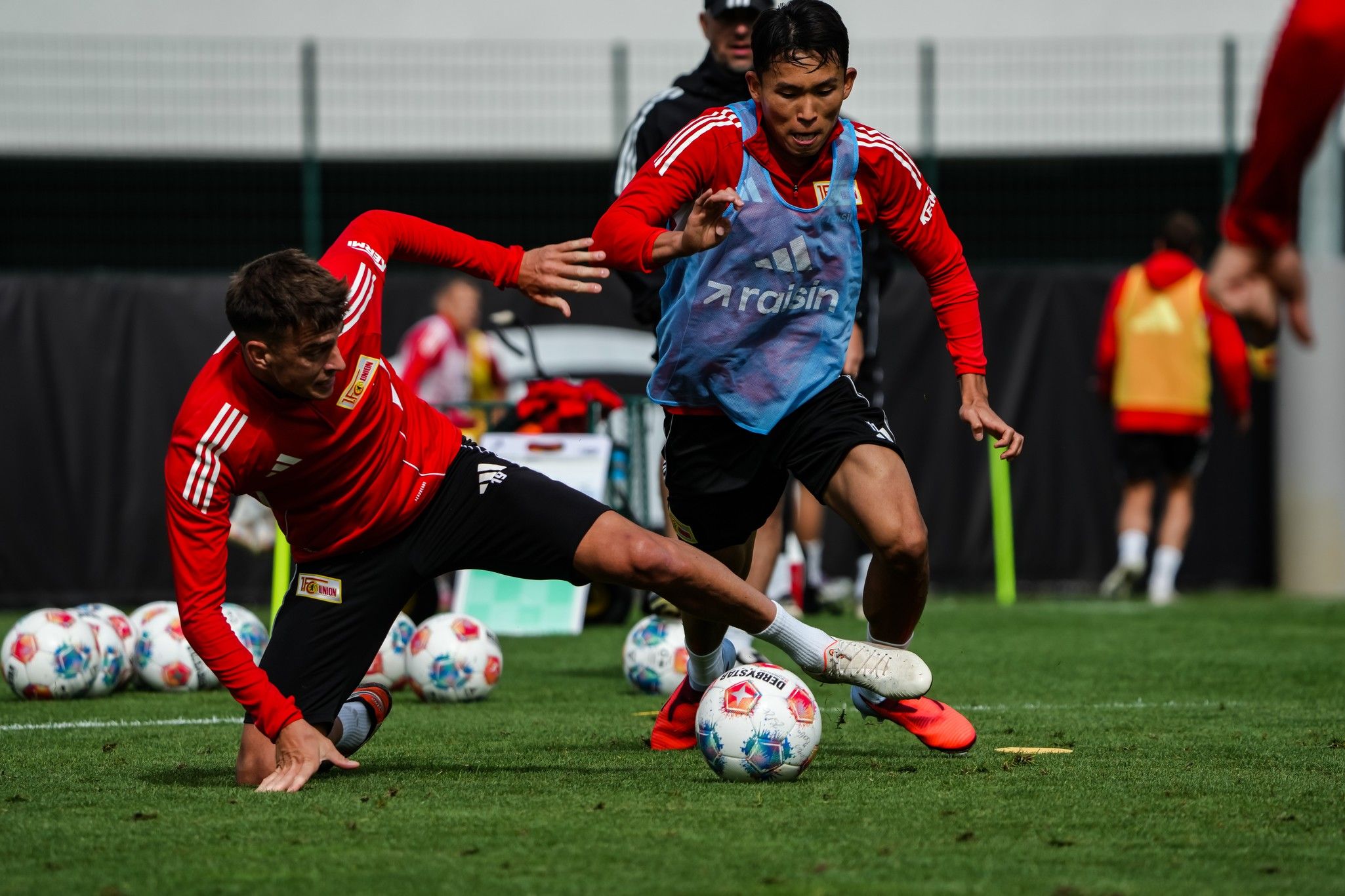 Zwei Fußballspieler trainieren auf einem Rasenplatz, während einer von ihnen im Fallen ist.