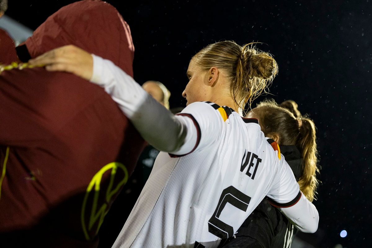Eine Fußballspielerin in einem weißen Trikot mit der Nummer 5 umarmt eine Teamkollegin nach einem Spiel, während es regnet.