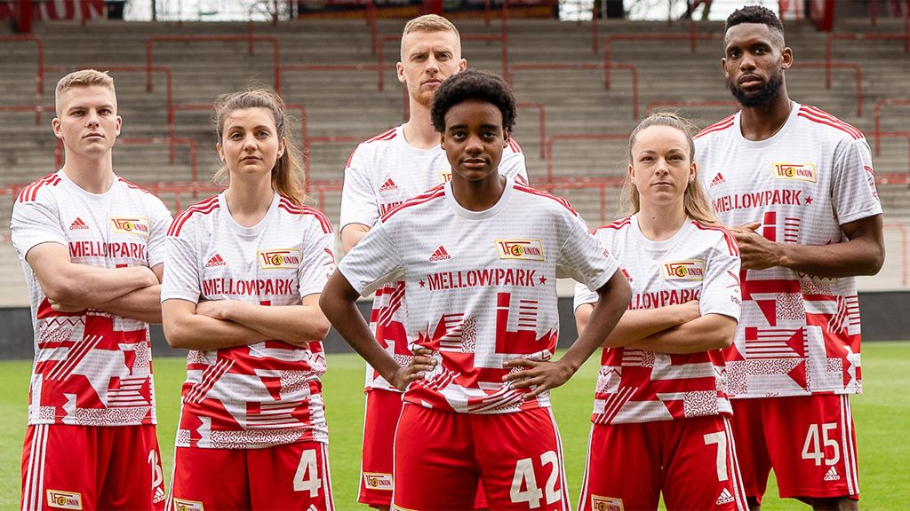 Sechs Fußballspieler in Trikots mit "Mellowpark" Logo stehen auf einem Sportfeld in einer lockeren Pose.