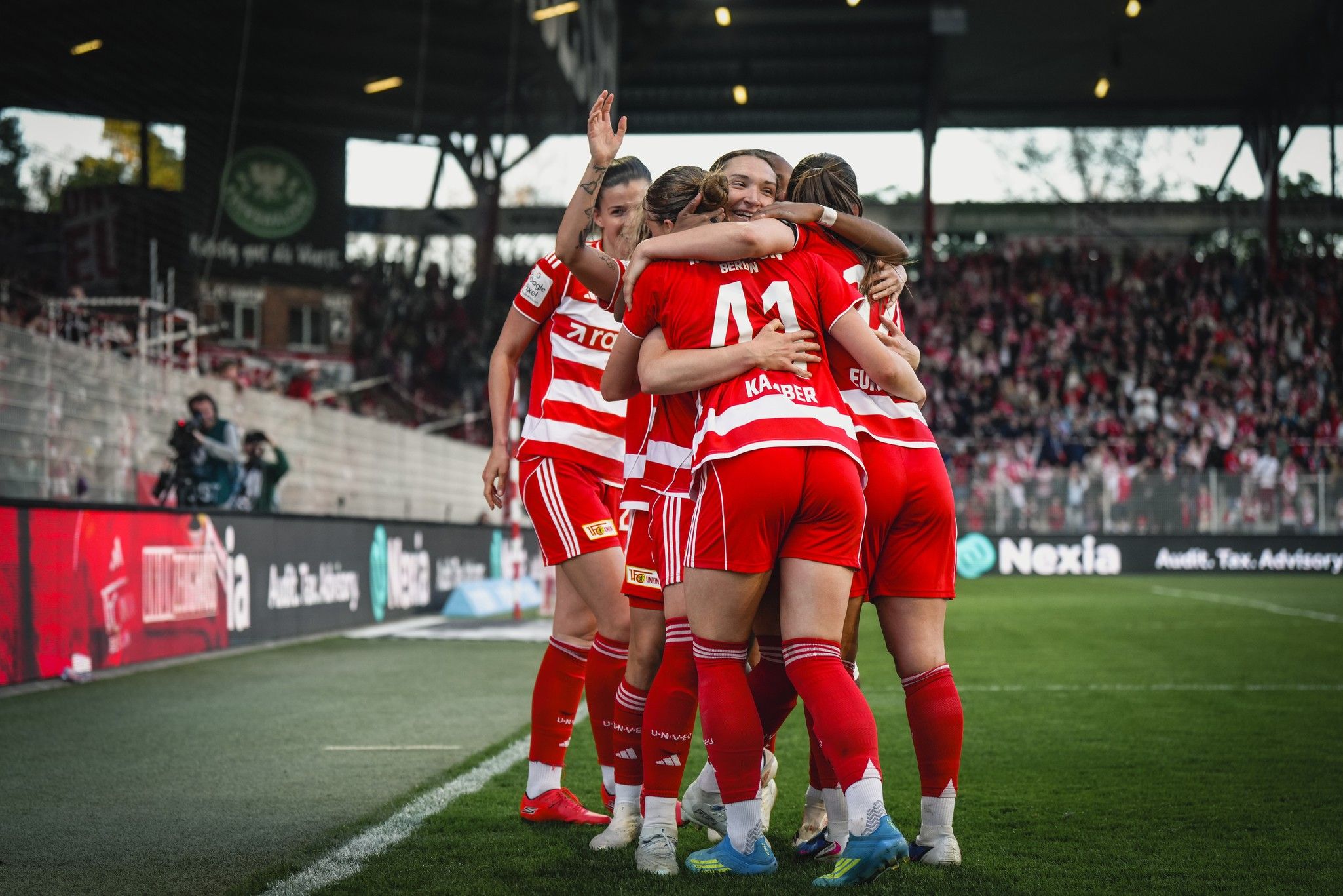 Ein Team von Fußballspielerinnen in roten Trikots feiert einen Torerfolg auf dem Spielfeld.
