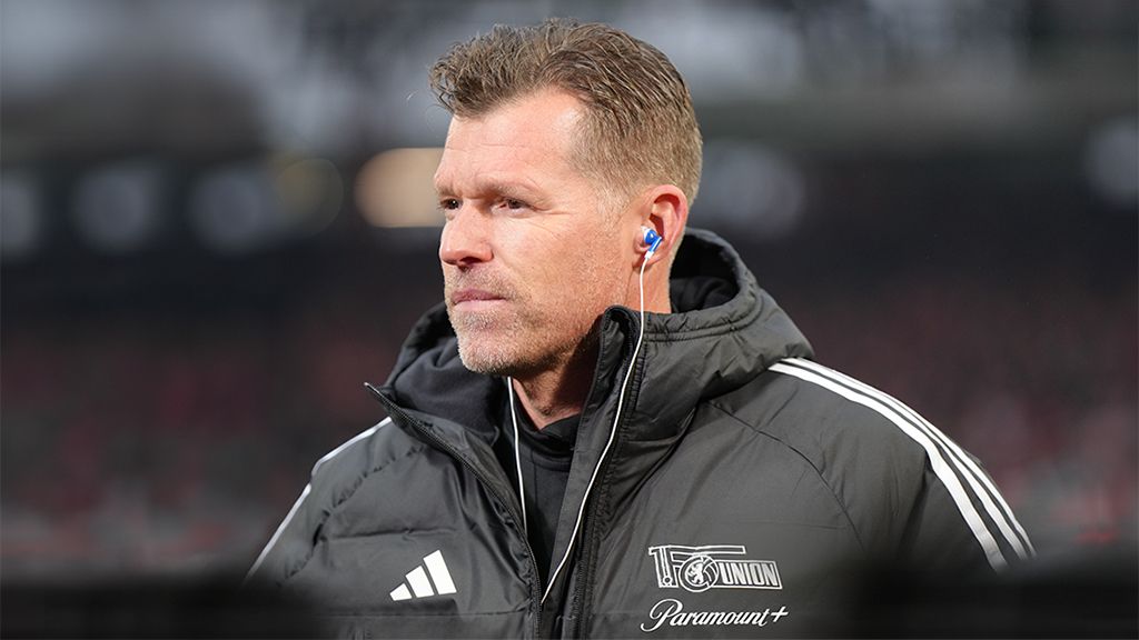 A coach in a black parka with headphones, focused on the game.