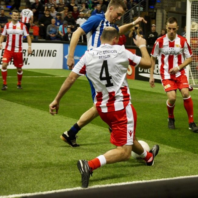 Zwei Fußballspieler im Wettkampf auf dem Spielfeld, einer rutscht in einer Abwehraktion, der andere hebt das Bein zum Schuss.