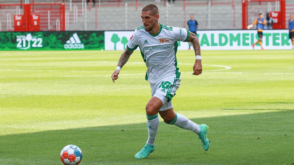 A soccer player in green and white uniform dribbles the ball on the field.
