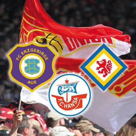 Ein Fan hält eine rote Fahne mit verschiedenen Fußballvereinslogos darauf, während im Hintergrund jubelnde Zuschauer zu sehen sind.