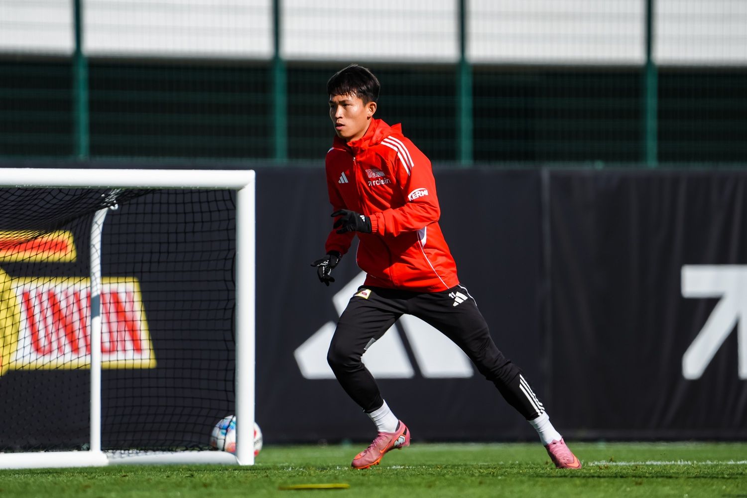 Ein Torwart in roter Trainingsjacke und schwarzen Hosen beim Training auf einem Fußballfeld.