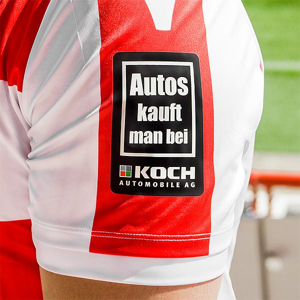 Das Bild zeigt einen Trikottafel mit einem roten und weißen Design sowie einem Werbeaufdruck für "Koch Automobile AG".