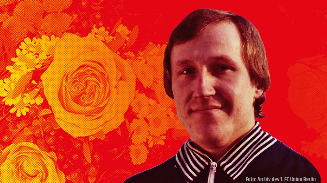 Ein lächelnder Mann vor einem bunten Hintergrund mit roten und orangen Rosenmotiven.