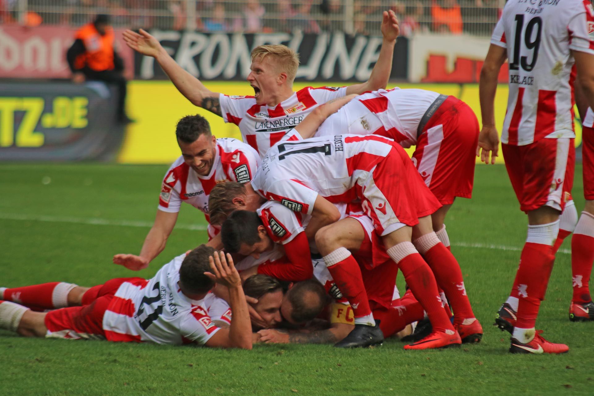 Eine Gruppe von Fußballspielern feiert einen Torerfolg, indem sie sich auf dem Feld umarmen und jubeln.