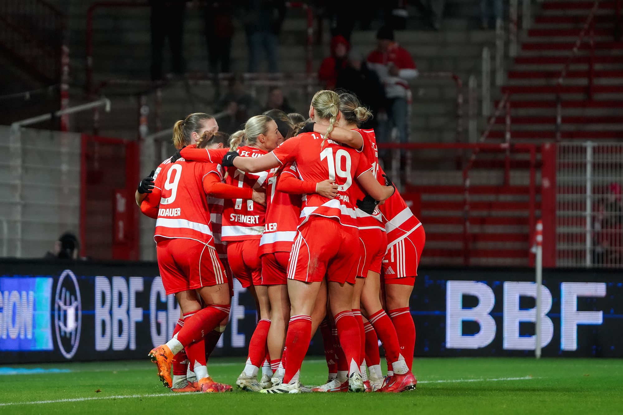 Spielerinnen einer Fußballmannschaft feiern einen Treffer und umarmen sich in einem Stadion.