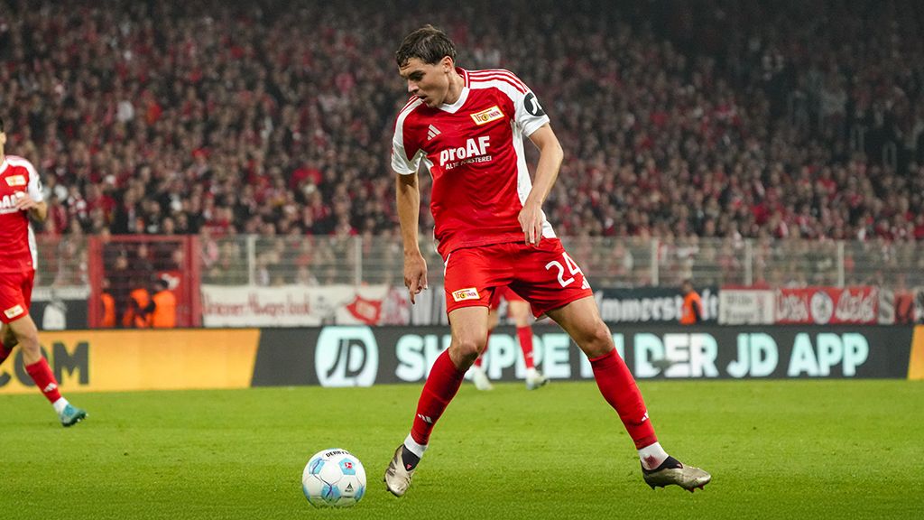 Ein Fußballspieler in rotem Trikot mit der Nummer 24 dribbelt den Ball vor einer jubelnden Menge im Stadion.
