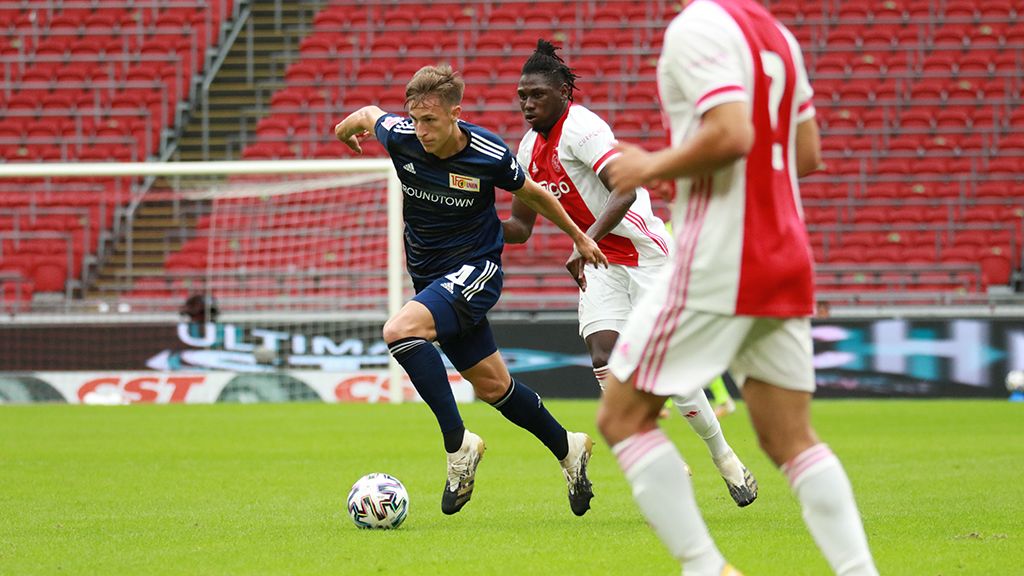 Zwei Fußballspieler in Aktion auf dem Platz, einer mit einer blauen, der andere mit einer weißen und roten Uniform.