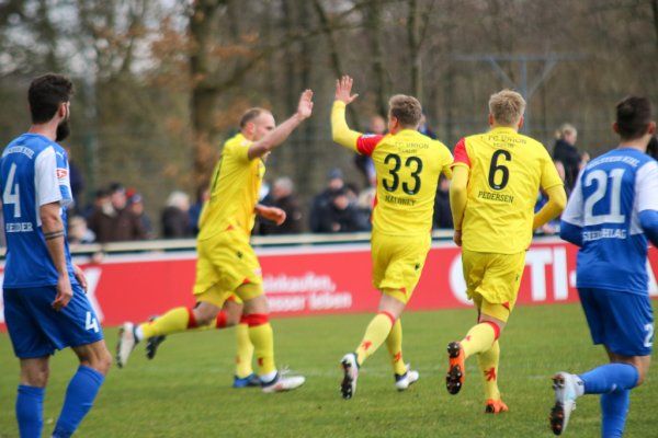 Spieler in gelben Trikots feiern ein Tor, während Spieler in blauen Trikots auf dem Platz stehen. Zuschauer im Hintergrund.