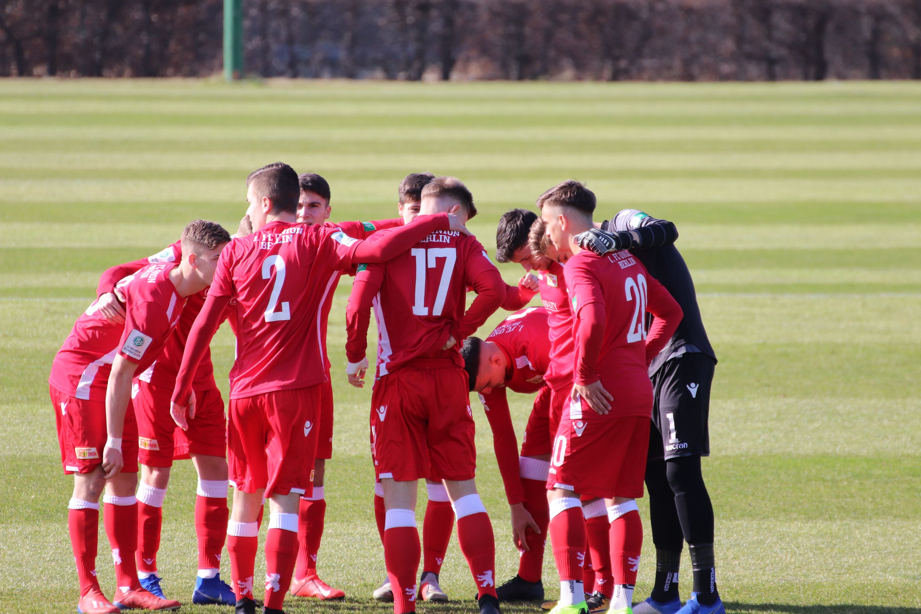 A group of football players in red jerseys gathers on the field for a team talk.