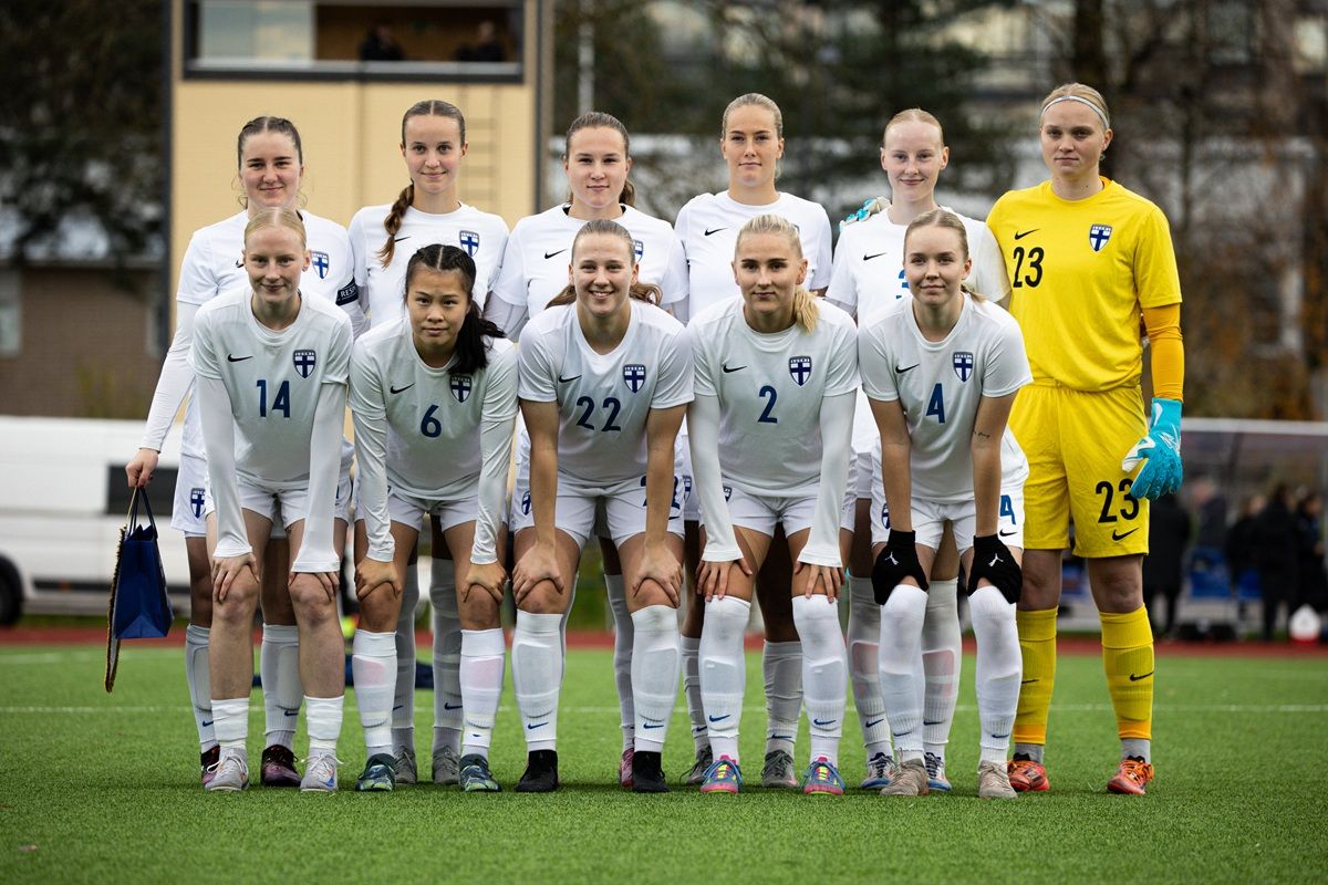 Eine Fußballmannschaft aus Frauen in weißen Trikots steht auf einem Spielfeld in aufrechter Position für ein Gruppenfoto.