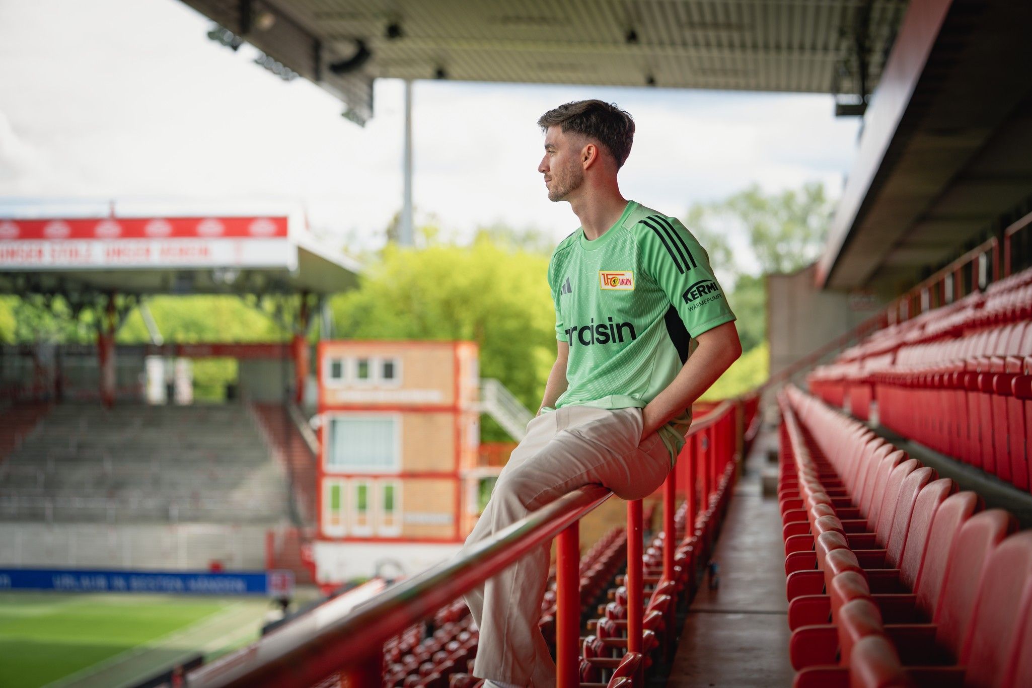 Ein junger Mann in einem Torwart-Trikot sitzt auf einer Stadionbalustrade und schaut nachdenklich in die Ferne.
