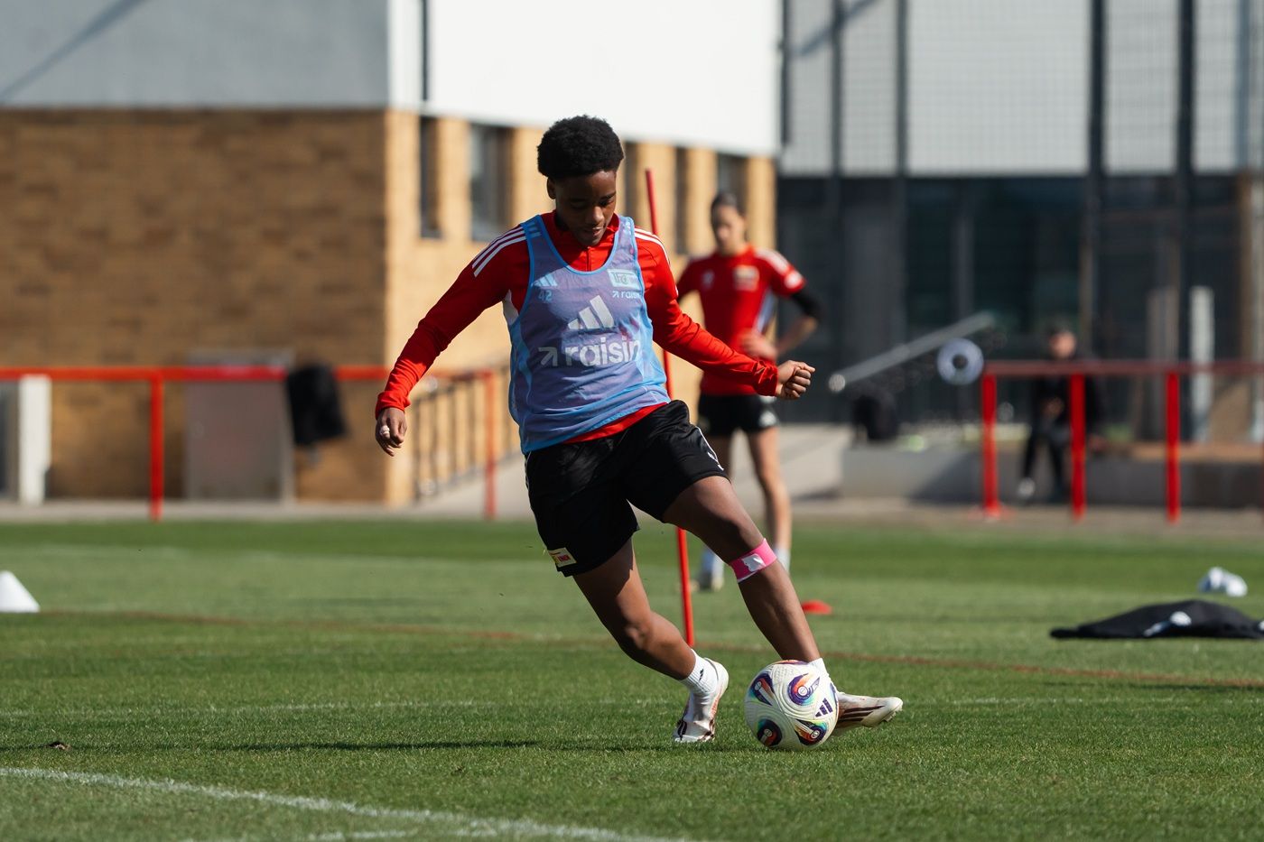Junger Fußballspieler in Trainingskleidung beim Ballspiel auf einem grünen Sportplatz.